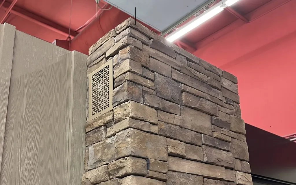 A decorative HVAC grille set into a stacked-stone façade column